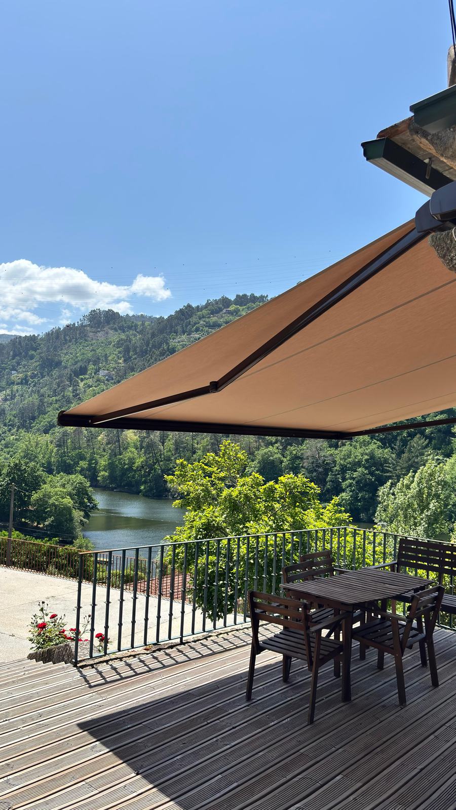 Toldo de braço articulado aberto sobre um deck de madeira com vista para o rio